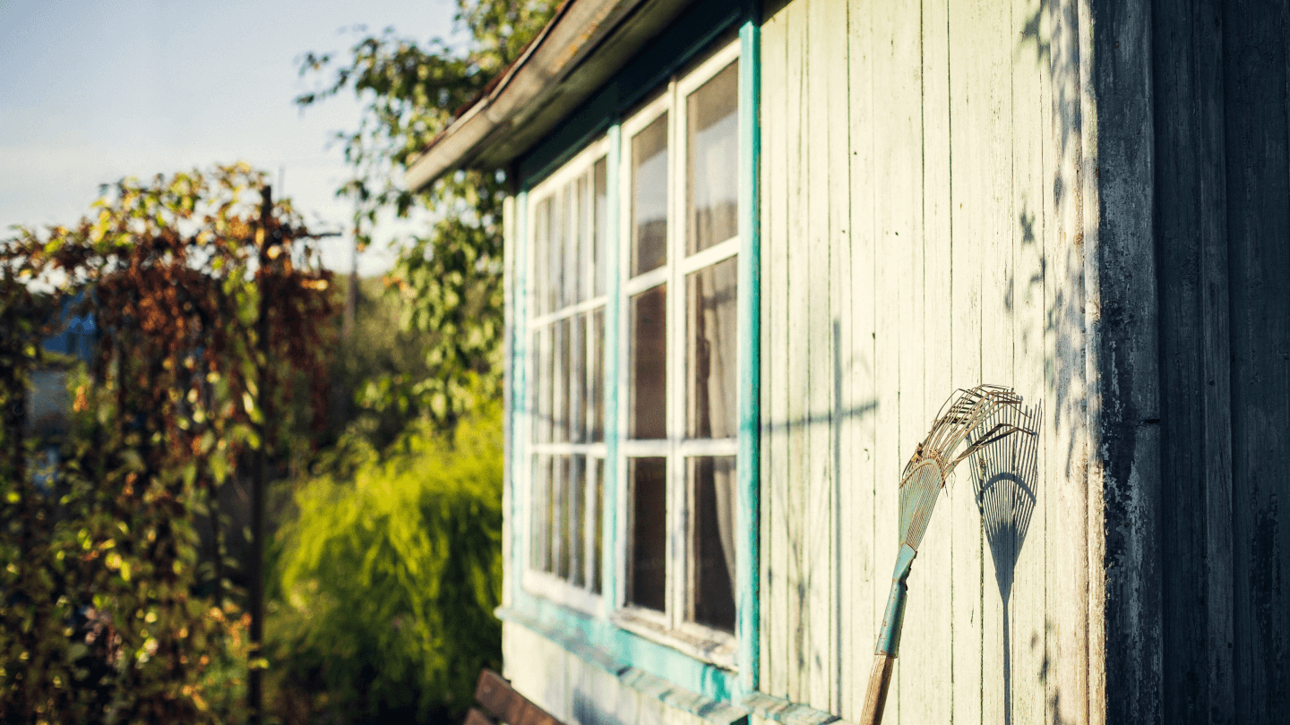 an old shed with a garden rake resting on it