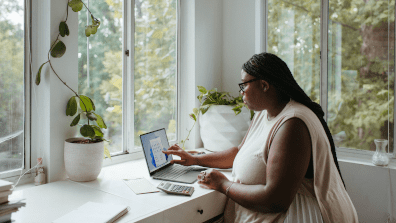 lady on laptop next to window with green vegetation outside