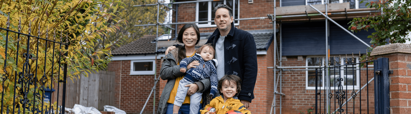 Man and Woman and 2 children stand outside a home that has scaffolding outside