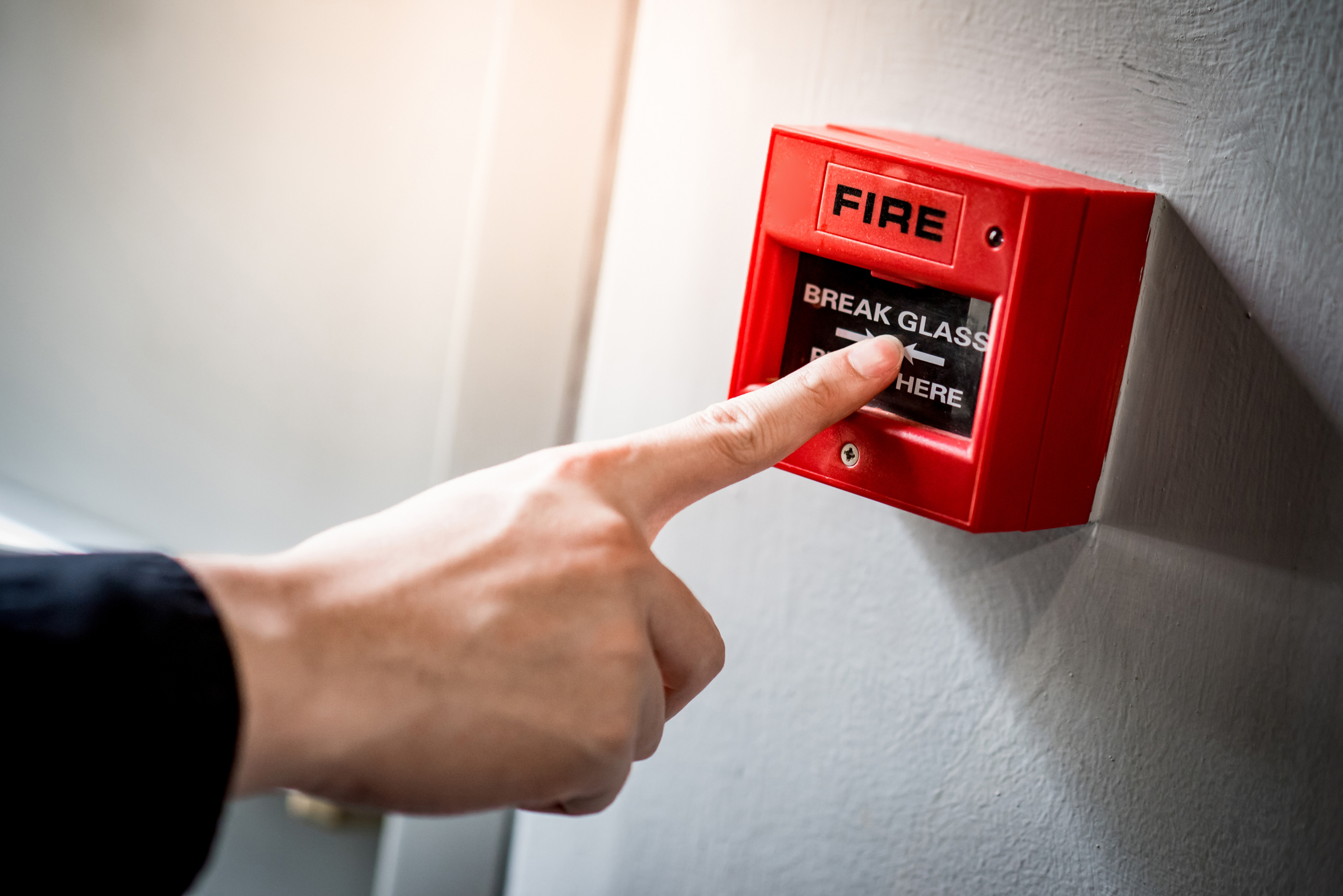 Person's hand pressing finger on fire alarm